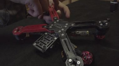 Parçalanmış FPV kuadrokopteri, siyah bir masanın üzerine kendin yap drone onarımı, eski plastik bir çerçevenin çıkarılması, kırık parçalar, İngiliz anahtarı ve tornavida ile sökülmesi, elektronik, mikro devreler, tamir, lehimleme.