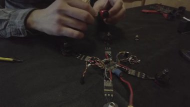 Parçalanmış FPV kuadrokopteri, siyah bir masanın üzerine kendin yap drone onarımı, eski plastik bir çerçevenin çıkarılması, kırık parçalar, İngiliz anahtarı ve tornavida ile sökülmesi, elektronik, mikro devreler, tamir, lehimleme.