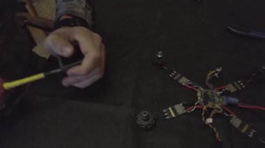 Parçalanmış FPV kuadrokopteri, siyah bir masanın üzerine kendin yap drone onarımı, eski plastik bir çerçevenin çıkarılması, kırık parçalar, İngiliz anahtarı ve tornavida ile sökülmesi, elektronik, mikro devreler, tamir, lehimleme.
