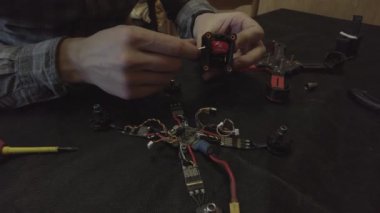 Parçalanmış FPV kuadrokopteri, siyah bir masanın üzerine kendin yap drone onarımı, eski plastik bir çerçevenin çıkarılması, kırık parçalar, İngiliz anahtarı ve tornavida ile sökülmesi, elektronik, mikro devreler, tamir, lehimleme.