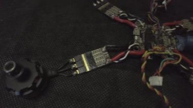 Parçalanmış FPV kuadrokopteri, siyah bir masanın üzerine kendin yap drone onarımı, eski plastik bir çerçevenin çıkarılması, kırık parçalar, İngiliz anahtarı ve tornavida ile sökülmesi, elektronik, mikro devreler, tamir, lehimleme.