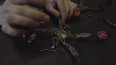 Parçalanmış FPV kuadrokopteri, siyah bir masanın üzerine kendin yap drone onarımı, eski plastik bir çerçevenin çıkarılması, kırık parçalar, İngiliz anahtarı ve tornavida ile sökülmesi, elektronik, mikro devreler, tamir, lehimleme.