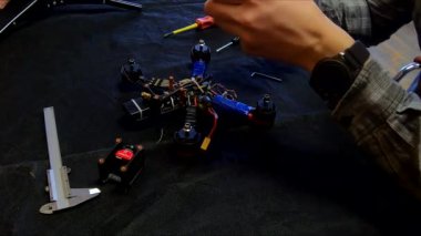Parçalanmış FPV kuadrokopteri, siyah bir masanın üzerine kendin yap drone onarımı, eski plastik bir çerçevenin çıkarılması, kırık parçalar, İngiliz anahtarı ve tornavida ile sökülmesi, elektronik, mikro devreler, tamir, lehimleme.