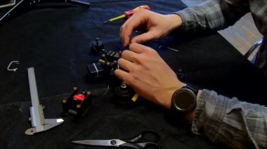 Parçalanmış FPV kuadrokopteri, siyah bir masanın üzerine kendin yap drone onarımı, eski plastik bir çerçevenin çıkarılması, kırık parçalar, İngiliz anahtarı ve tornavida ile sökülmesi, elektronik, mikro devreler, tamir, lehimleme.