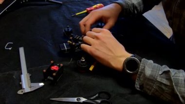 Parçalanmış FPV kuadrokopteri, siyah bir masanın üzerine kendin yap drone onarımı, eski plastik bir çerçevenin çıkarılması, kırık parçalar, İngiliz anahtarı ve tornavida ile sökülmesi, elektronik, mikro devreler, tamir, lehimleme.