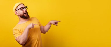 Gözlüklü gülümseyen sakallı adam işaret parmağı ile sarı arkaplan üzerinde, metin için yeri olan panoramik düzenek