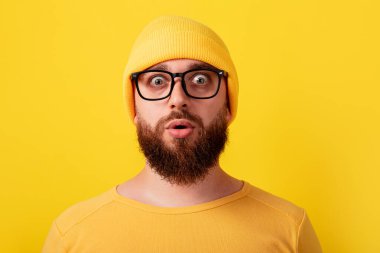 Şaşırmış bir adam sarı arka planda gözlük takıyor.