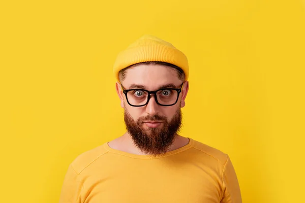 man with crazy look over yellow background, bearded guy looking into camera