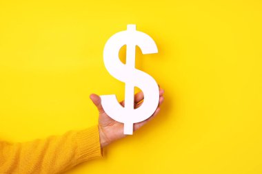 El ele tutuşan dolar sembolü sarı arka planda, finansal konsept