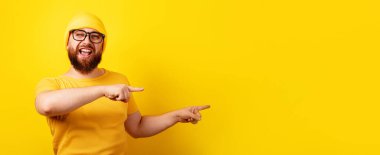 Gözlüklü gülümseyen sakallı adam işaret parmağı ile sarı arkaplan üzerinde, metin için yeri olan panoramik düzenek