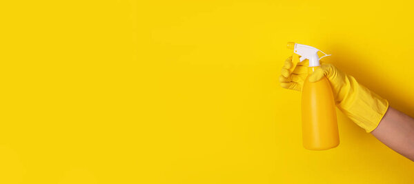 hand in a glove holding a spray bottle over yellow background, cleanliness concept, panoramic layout