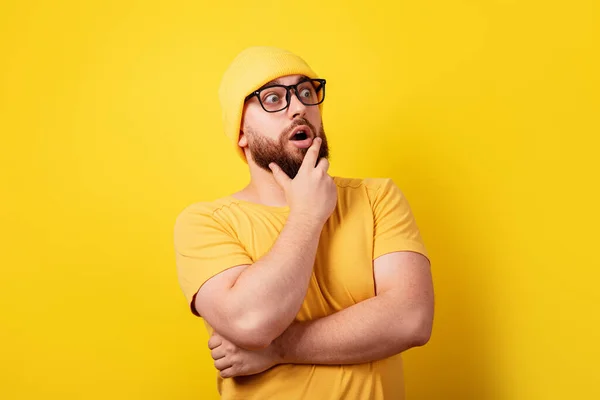 shocked thinking man in glasses looking aside over yellow background