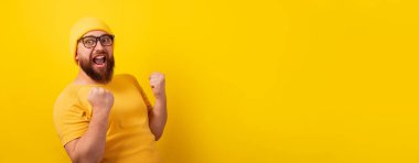 Sarı arka planda başarılı sakallı adam, kazanan jest, panoramik düzen