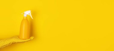 Sarı arka planda sprey şişesi tutan bir eldiven, temizlik konsepti, panoramik düzen