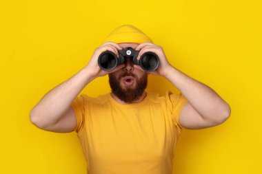 surprised man looking into binoculars over yellow background