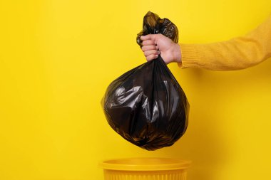 hand holding garbage bag over yellow background