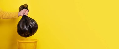 hand holding garbage bag over yellow background, panoramic layout