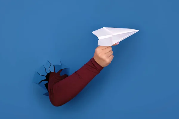 hand holding paper airplane over blue background