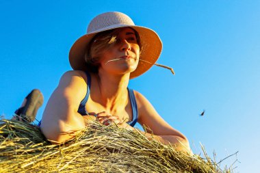 Açık arazide samanlıkta dinlenen bir kız.