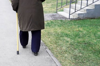 Yaşlı bir adam sopayla sokakta yürüyor.