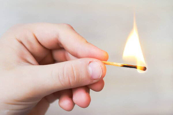 the child holds a lit match and it burns with a flame