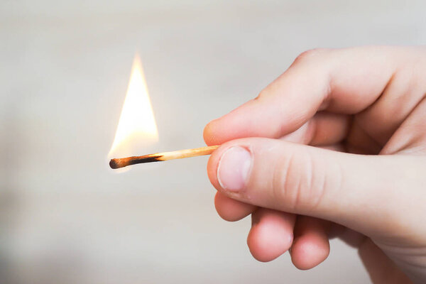 the child holds a lit match and it burns with a flame