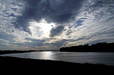 Günbatımı karanlık, hatta gri gökyüzü bile nehrin arka planında ve sık yeşillik yazın orman ve çimen şeklinde.