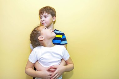 Erkek ve kız kardeşler sarı duvara karşı yan yana dururlar, sarılırlar ve farklı görünürler. Aile dostluğu