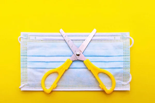 medical mask and scissors lie on a yellow background shown from top to bottom close-up. covid-19. without vaccination