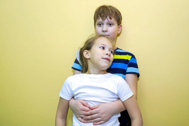 Erkek ve kız kardeşler sarı duvara karşı yan yana dururlar, sarılırlar ve farklı görünürler. Aile dostluğu