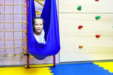 Beyaz dar elbiseli küçük kız hamakta spor yapmak için yoga sınıfındaki gibi denge ve denge kuruyor.