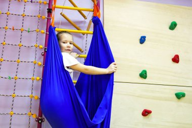 Beyaz dar elbiseli küçük kız hamakta spor yapmak için yoga sınıfındaki gibi denge ve denge kuruyor.