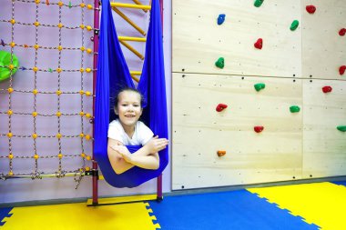 Beyaz dar elbiseli küçük kız hamakta spor yapmak için yoga sınıfındaki gibi denge ve denge kuruyor.