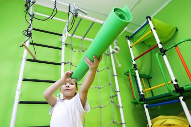 Büyük merakı olan küçük bir kız dürbün gibi spor aktiviteleri için lastik bir paspasın içine bakar.