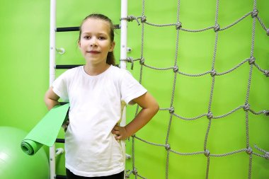 Özel giyinmiş küçük bir kız lastik bir paspasın üzerinde spor yapmaya gider ve donanımlı bir çocuk merkezinde sağlıklı bir hayat sürer.