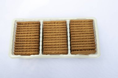 Plastik tepside bulunan kahverengi buğday bisküvileri arka planda izole edilmiş.