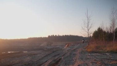 Erkek motokros sürücüsü gün batımında Ekstrem off-road yolunda FMX motorsikletine biniyor.