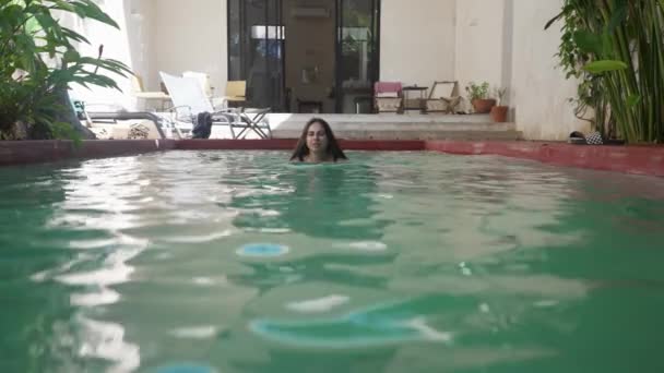 Vrouw zwemt in een zwembad met water in een villa in de zomer op een zonnige dag — Stockvideo