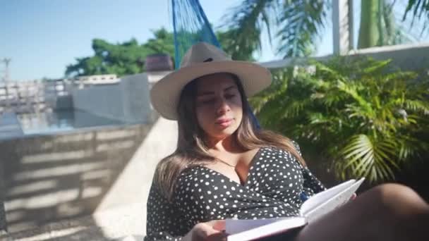 Young woman relaxed reading a book in a hammock in a rooftop next to pool — Stock Video
