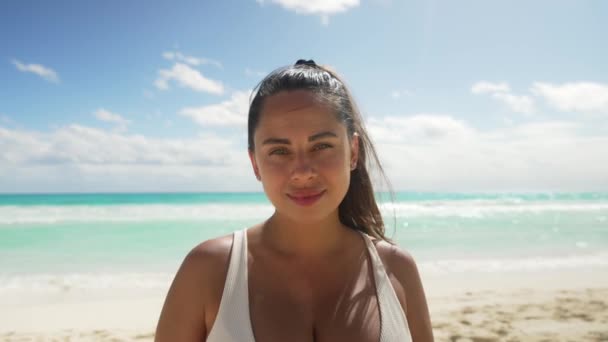 Glad ung kvinna som står vid Cancun Beach. Känslig kvinna med vindpinat hår tittar på kameran. Hon bär vit bikini topp under sommarlovet på Cancun Mexico. — Stockvideo