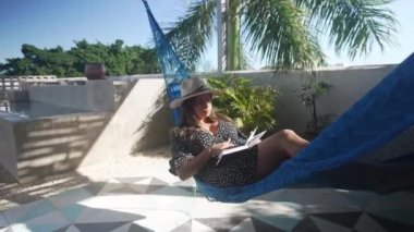 Genç bir kadın, havuzun yanındaki bir hamakta kitap okurken rahatladı.