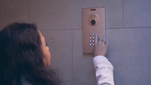 Menina espanhola jovem pressiona botões no teclado numérico de vídeo Intercom instalado na parede interior amarrada. dolly-out — Vídeo de Stock