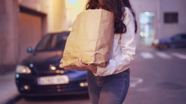 Chica va a casa sosteniendo bolsa de papel marrón con productos después de comprar. - de cerca — Vídeo de stock