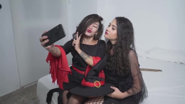 Dvě atraktivní kolumbijské ženy v černých kostýmech čarodějnice, které berou Selfies pomocí Smartphone v ložnici bytu ve Valencii, Španělsko. - Střední výstřel — Stock video
