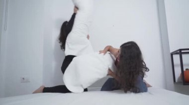 İki arkadaş beyaz yatakta yastık kavgası yapıyor. geniş çekim