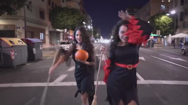 Dwie ładne dziewczyny spacerujące po pustej drodze w kostiumach Halloween - poruszające się średnie ujęcie — Wideo stockowe