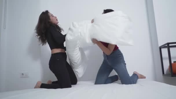Dos mujeres riendo mientras almohada luchando en la cama. plano medio — Vídeos de Stock