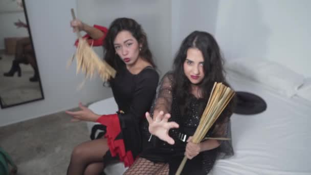 Vonzó hölgyek fekete boszorkány jelmezek szórakozás boszorkányok seprűk a hálószobában, miközben néz fel a kamerába. magas szög — Stock videók