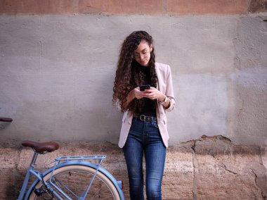 Duvarın karşısında cep telefonu kullanan yetişkin bir kadın