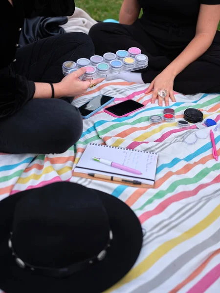 Two young women sitting with legs crossed, one of them picking up the paints — Fotografia de Stock